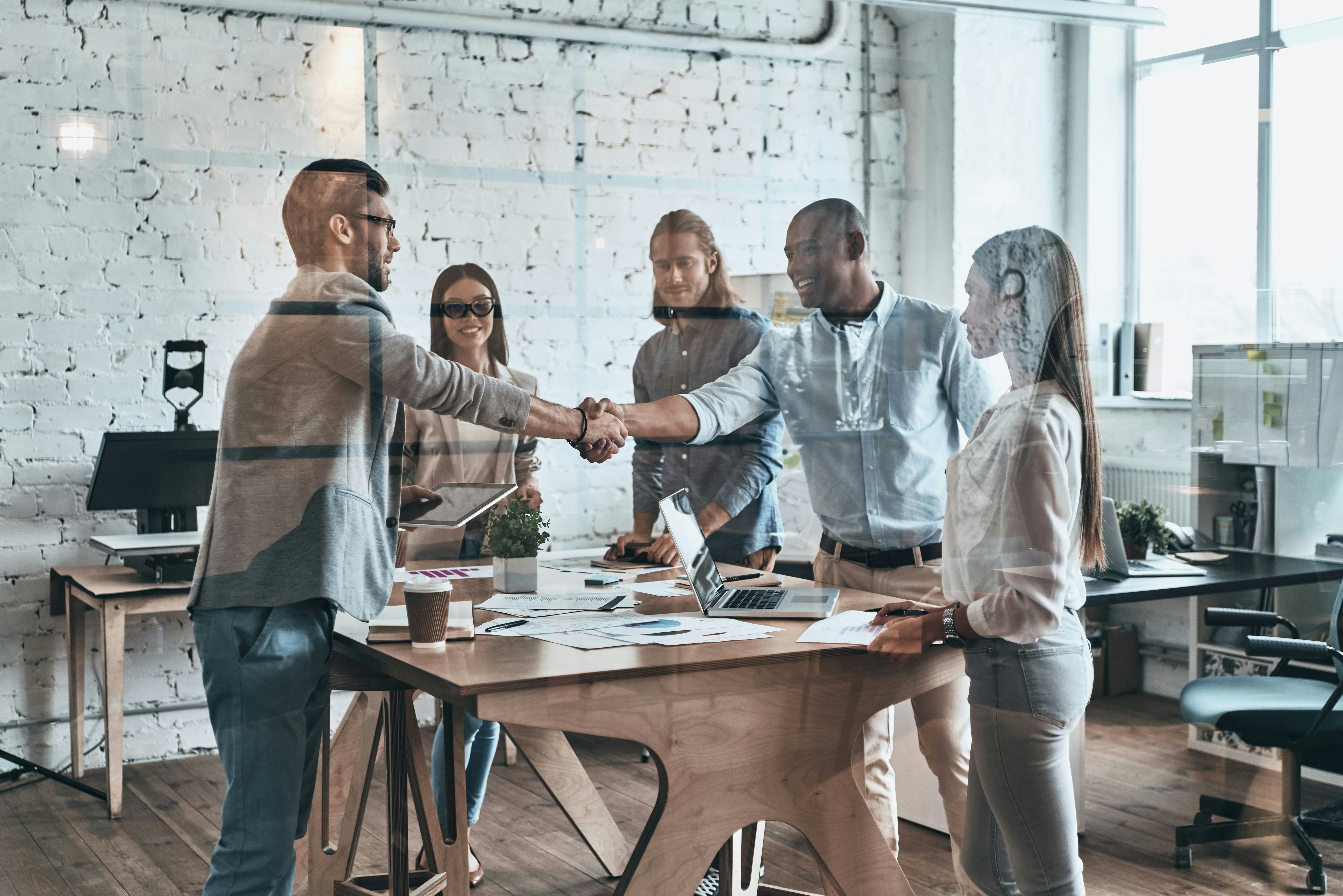 Colleagues shaking hands in an office with three other colleagues standing around the table